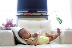 Self feeding baby ,baby drinking milk comfortably lying down on a sofa.