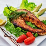 Grilled fish served with green vegetables avocado and orange....
