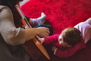 mother playing a guitar for her baby in I month old baby activities on a baby activity table