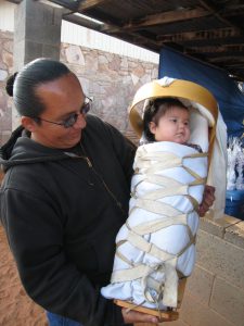 Father holding baby in a Native American baby carrier  