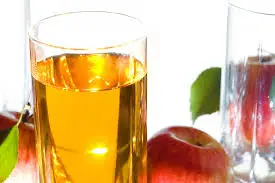 Glass jar with apple white grape juice and some fresh grapes and apples beside it .