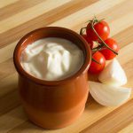 Tomatoes and onions on a table with cup full of sour cream